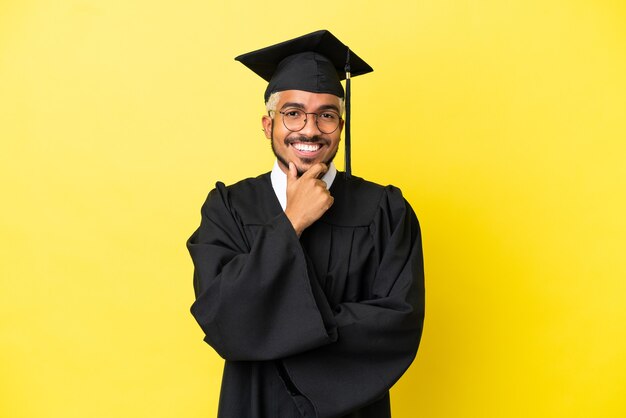 Young university graduate Colombian man isolated on yellow background with glasses and smiling