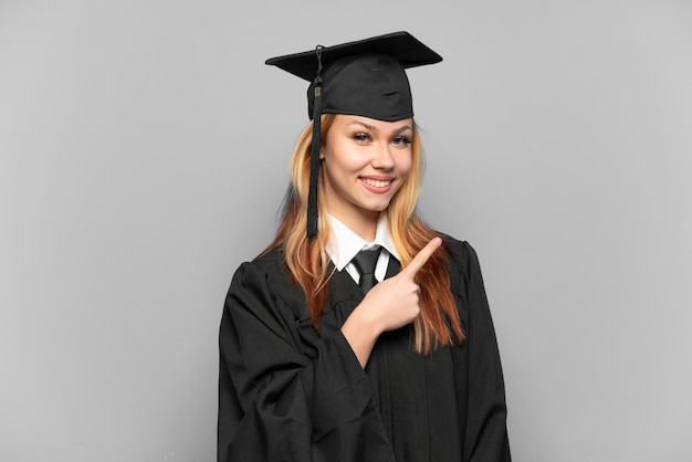 Young university graduate girl over isolated background pointing to the side to present a product