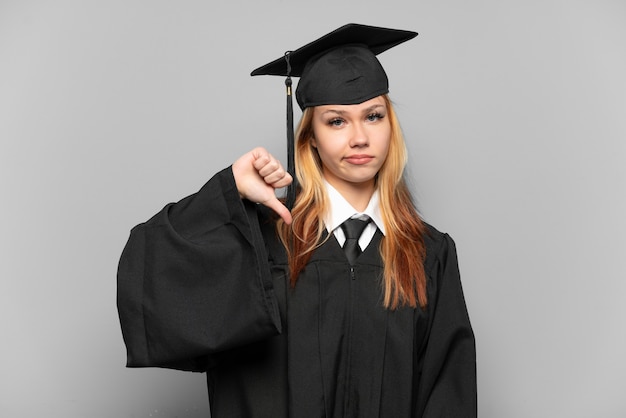 Молодая девушка-выпускница университета на изолированном фоне показывает большой палец вниз с отрицательным выражением лица