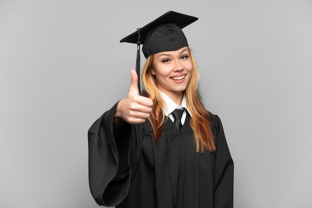 Foto ragazza giovane laureata universitaria su sfondo isolato con i pollici in su perché è successo qualcosa di buono