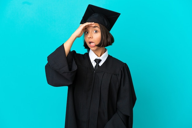 Young university graduate girl over isolated blue background doing surprise gesture while looking to the side