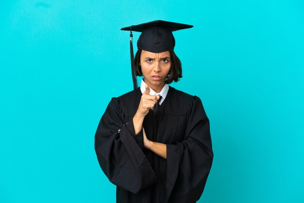 Young university graduate girl over isolated blue background frustrated and pointing to the front