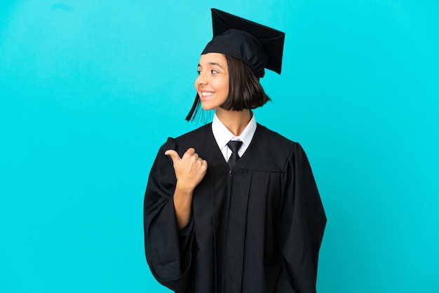 Молодая девушка-выпускница университета на изолированном синем фоне, указывая в сторону, чтобы представить продукт