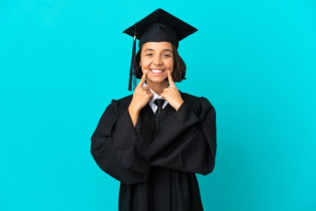 幸せで楽しい表情で笑って孤立した青い背景の上の若い大学卒業生の女の子