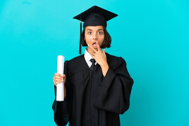 Young university graduate girl over isolated blue background surprised and shocked while looking right