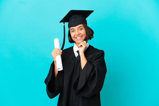 笑っている孤立した青い壁の上の若い大学卒業生の女の子