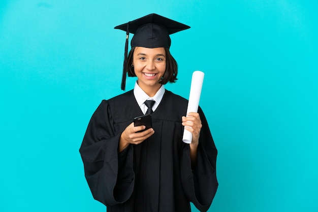 Young university graduate girl over isolated blue wall sending a message with the mobile