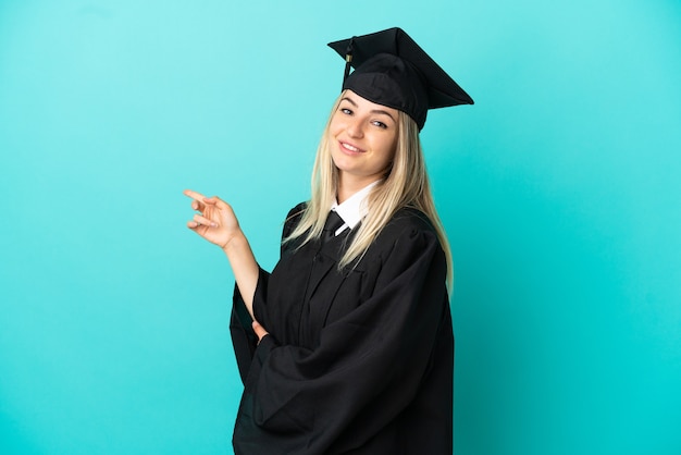 Young university graduate over isolated blue background pointing finger to the side