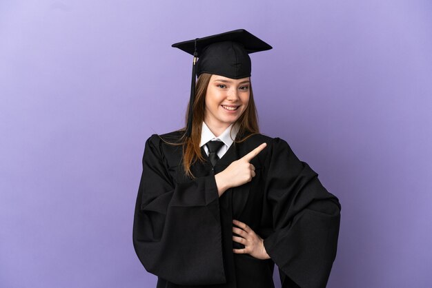 Young university graduate over isolated purple background pointing to the side to present a product