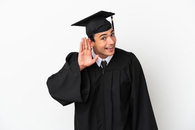 若い大学は、耳に手を置いて何かを聞いて孤立した白い背景の上に卒業します