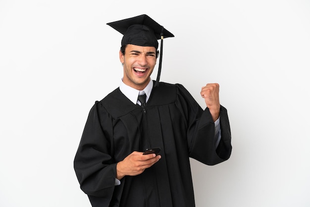 Young university graduate over isolated white background with phone in victory position