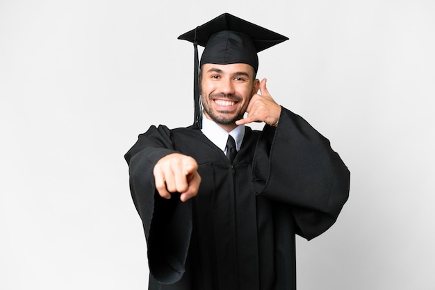 Молодой выпускник университета на изолированном белом фоне делает телефонный жест и указывает вперед