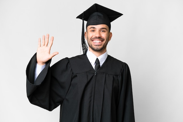 Young university graduate man over isolated white background saluting with hand with happy expression