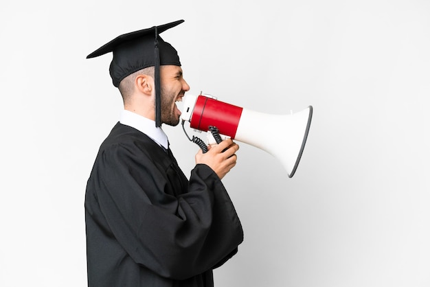 Young university graduate man over isolated white background shouting through a megaphone