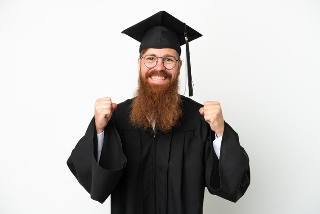 Young university graduate reddish man isolated on white background celebrating a victory in winner position