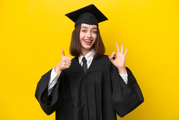 Young university graduate Ukrainian woman isolated on yellow background showing ok sign and thumb up gesture