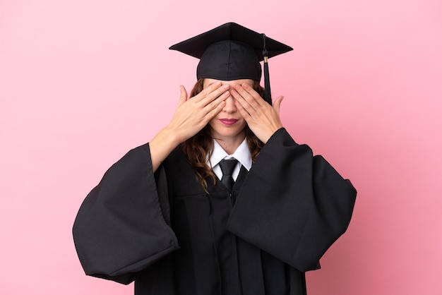 Young university graduate woman isolated on pink background covering eyes by hands