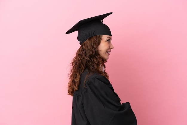 Giovane donna laureata isolata su sfondo rosa in posizione laterale