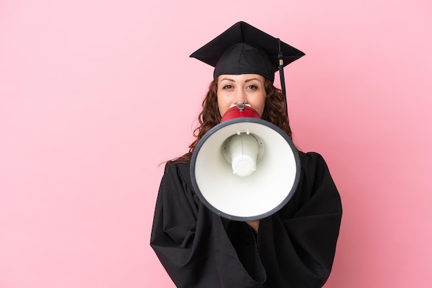 メガホンを介して叫んでピンクの背景に分離された若い大学卒業生の女性