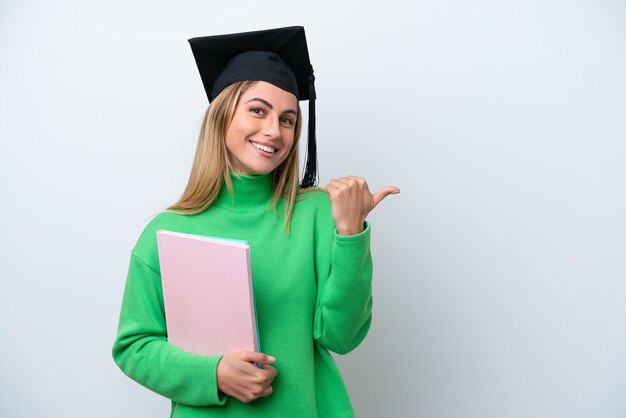 Young university graduate woman isolated on white background\
pointing to the side to present a product