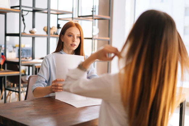 写真 向かい合った机に座って成功したスタートアップについて会話しているデザイン会社での仕事のためにインタビューされている若い認識できない建築家の学生