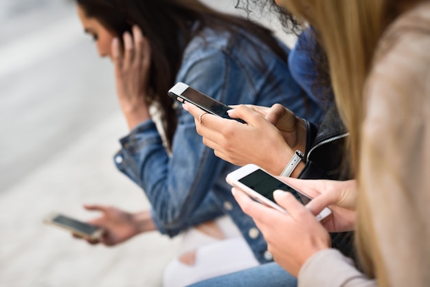 Young unrecognizable people using smartphone and tablet computers outdoors