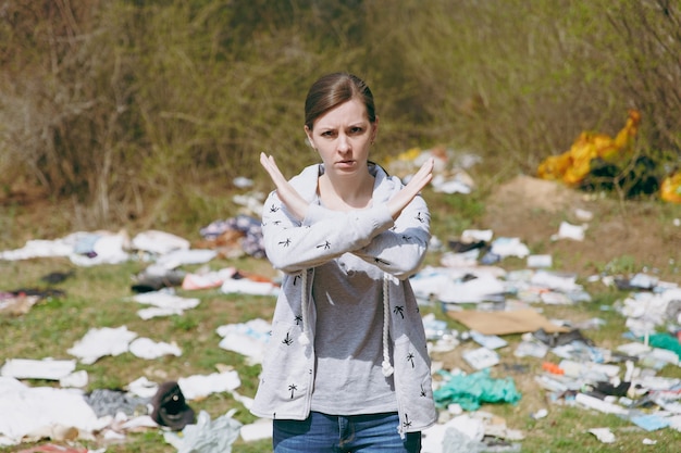 Young upset concerned woman in casual clothes cleaning showing stop gesture with crossed hands in littered park