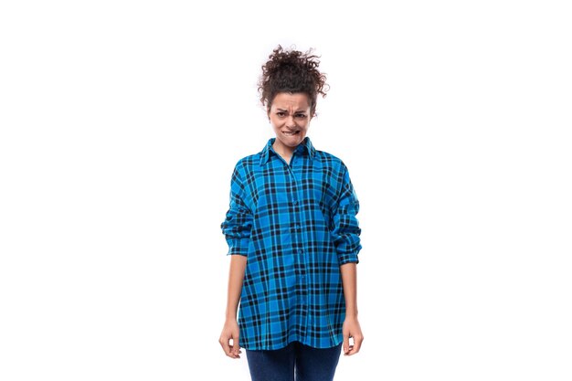 Young upset curly brunette woman in a blue plaid shirt on a white background