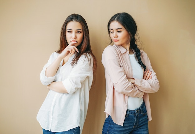 Young upset girls friends in casual offended at each other isolated on beige background, jealousy concept