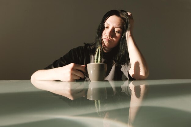 Foto giovane donna sconvolta con una maglietta grigia tiene in mano una tazza di caffè con un cactus
