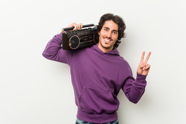 Young urban man holding a guetto blaster joyful and carefree showing a peace symbol with fingers.