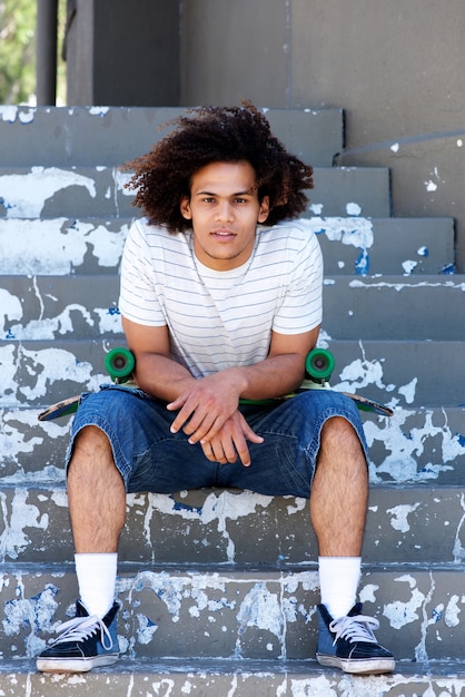 Photo young urban man sitting on steps with skateboard