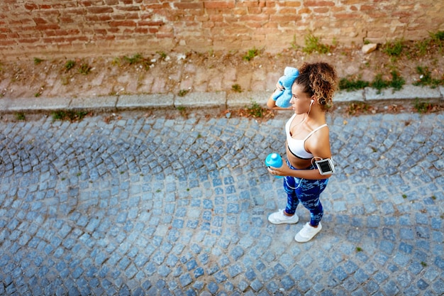 Young urban runner woman with headphones resting after jogging.