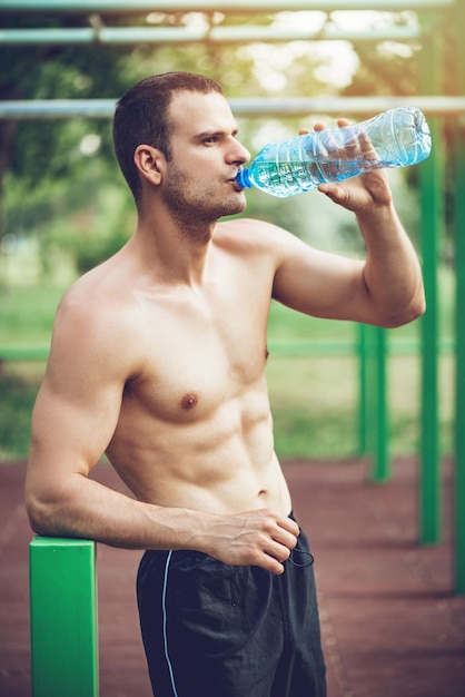 Young urban sportsman drinking water after hard training in the nature.