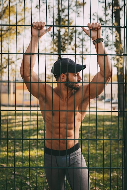 Young urban sportsman with headphones resting after training in the park and looking away.