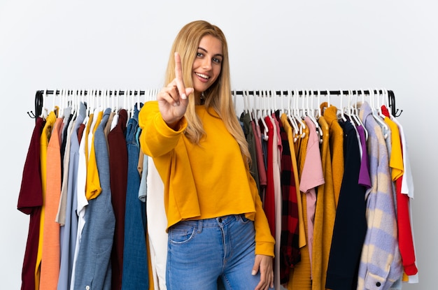 Young Uruguayan blonde woman in a clothing store showing and lifting a finger