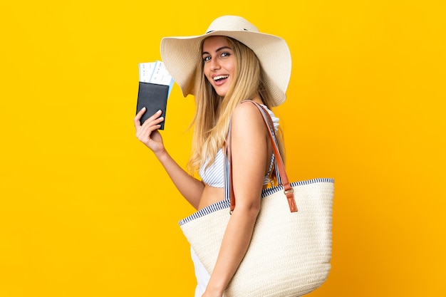 Young Uruguayan blonde woman in swimsuit holding a passport over isolated yellow background smiling a lot