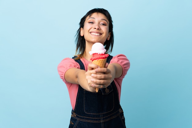 Giovane ragazza uruguaiana che tiene un gelato della cornetta sopra il blu isolato