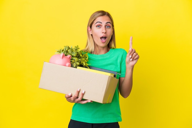 Young Uruguayan girl making a move while picking up a box full of things isolated on yellow background intending to realizes the solution while lifting a finger up