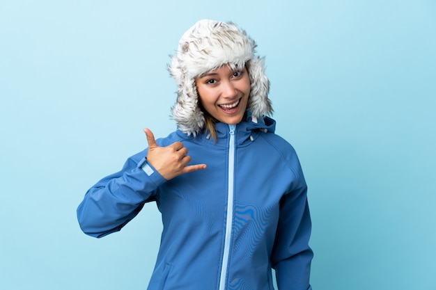 Young Uruguayan girl with winter hat isolated on blue making phone gesture