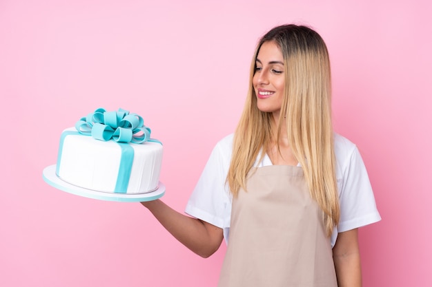 Young Uruguayan pastry woman with a big cake with happy expression