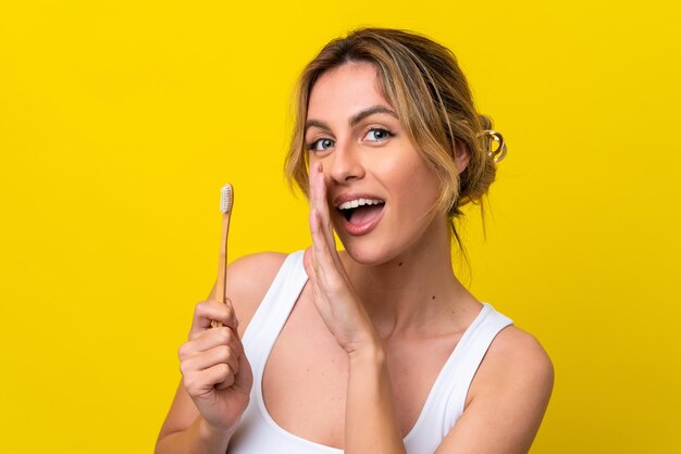 Foto giovane donna uruguaiana che lava i denti isolati su sfondo giallo che sussurra qualcosa