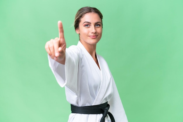 Young Uruguayan woman doing karate over isolated background showing and lifting a finger