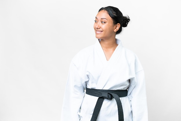 Young Uruguayan woman doing karate over isolated white background looking to the side and smiling