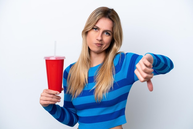 Young uruguayan woman drinking soda isolated on white\
background showing thumb down with negative expression