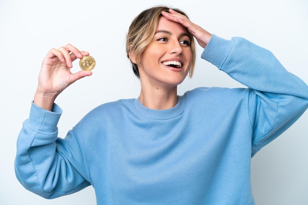 Young Uruguayan woman holding a Bitcoin isolated on white background smiling a lot