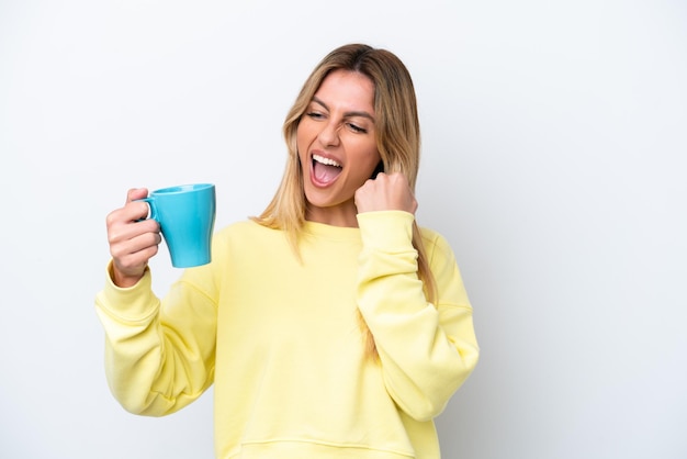 Young Uruguayan woman holding cup of coffee isolated on white background celebrating a victory