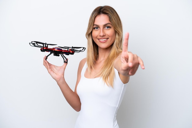 Foto giovane donna uruguaiana che tiene un drone isolato su sfondo bianco che mostra e alza un dito