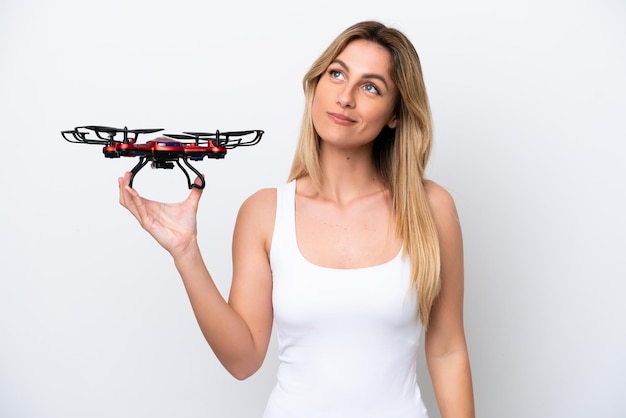 Giovane donna uruguaiana che tiene un drone isolato su sfondo bianco pensando a un'idea mentre guarda in alto