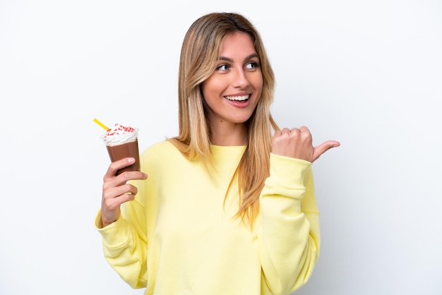 Young Uruguayan woman holding Frappuccino isolated on white background pointing to the side to present a product